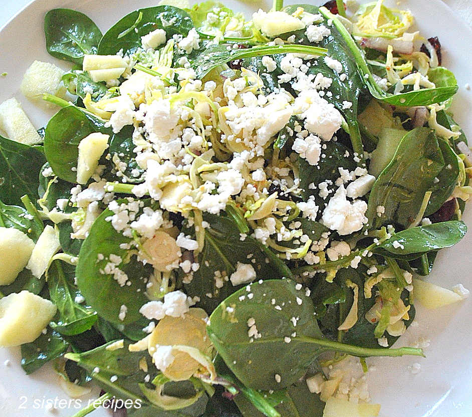 A mix of greens with crumbled cheese on top served on a white dinner plate.