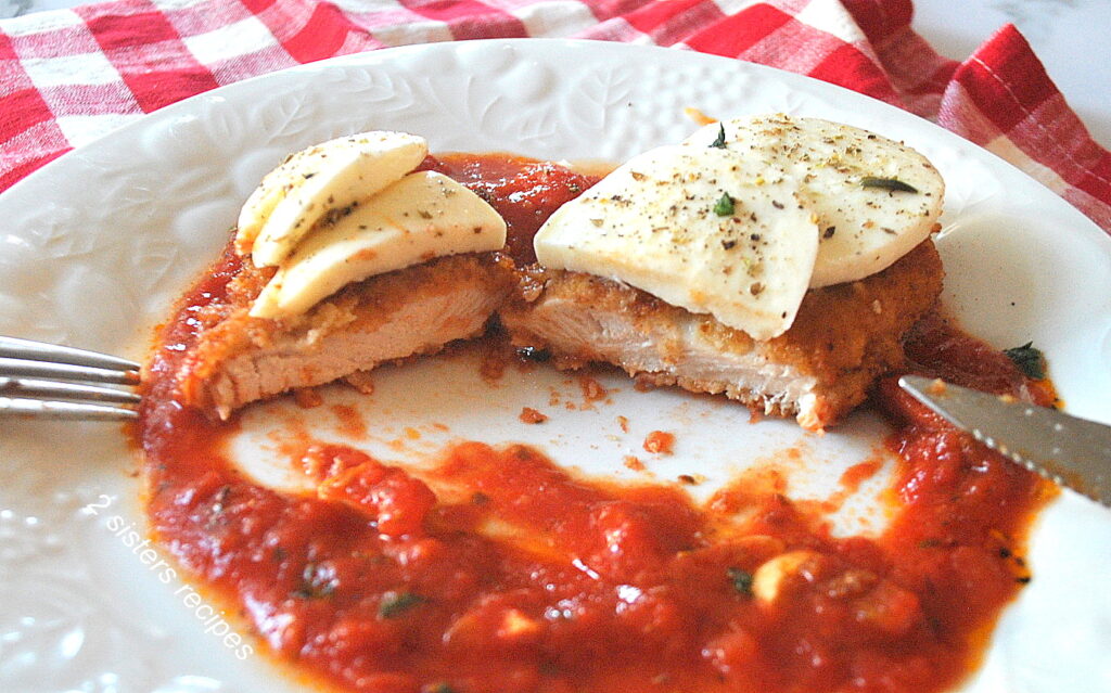 A dinner plate with a chicken cutlet over pizza sauce, and topped with fresh mozzarella sliced in half.