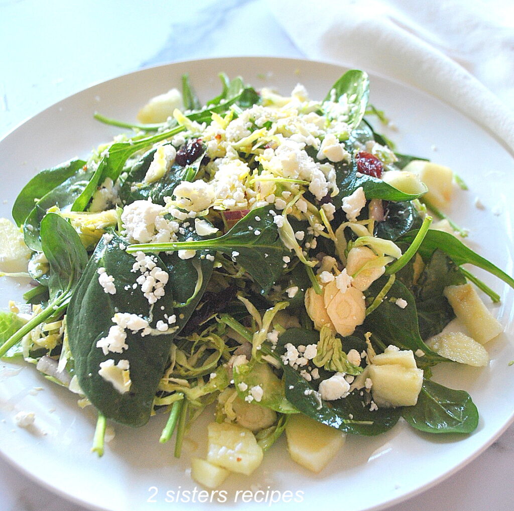 A white plate with fresh green salad, topped with crumbled goat cheese.