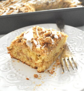 A piece of apple crumb coffee cake served on a white plate with a fork on the side.
