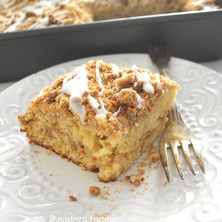 A piece of apple crumb coffee cake served on a white plate with a fork on the side.