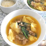 A white bowl filled with Tortellini, spinach and crumbled sausage soup.