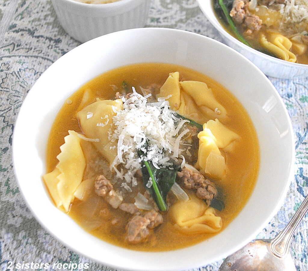 A white bowl filled with tortellini and sausage soup with grated cheese on top.