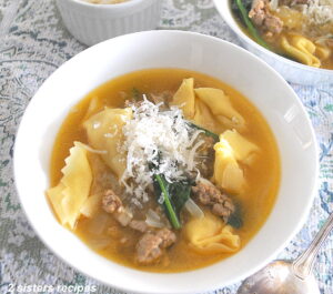 A white bowl filled with tortellini and sausage soup with grated cheese on top.