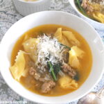 A white bowl filled with Tortellini and crumbled sausage soup with grated cheese on top.