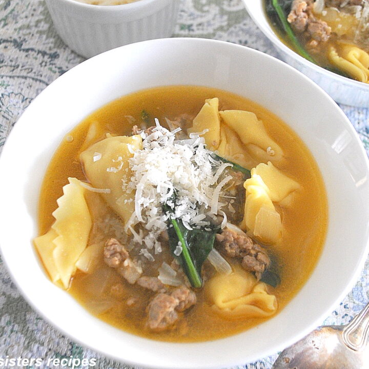 A white bowl filled with Tortellini and crumbled sausage soup with grated cheese on top.