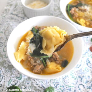 A spoonful of tortellini, sausage and spinach soup over a white bowl.