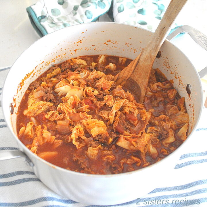 A white Dutch oven pot filled with cabbage and ground beef stew and a wooden spoon inside.