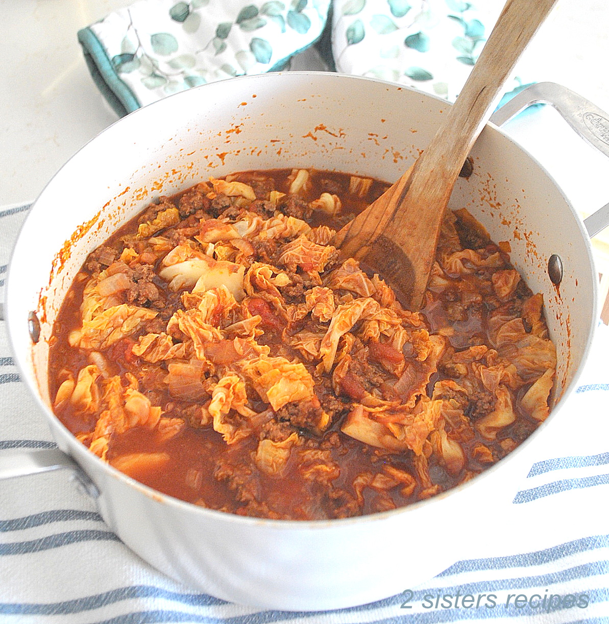 A white Dutch oven pot filled with cabbage and ground beef stew and a wooden spoon inside.