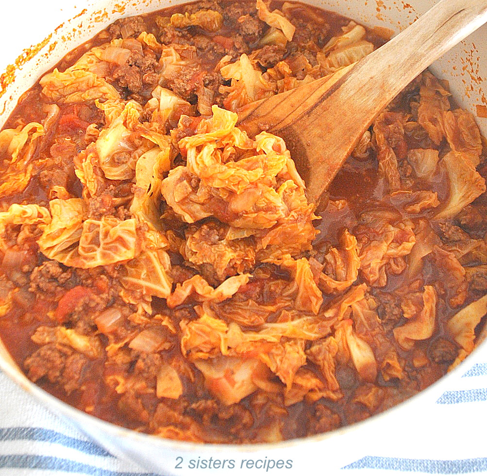 A pot filled with cooked cabbage with ground beef and a wooden spoon stirring.