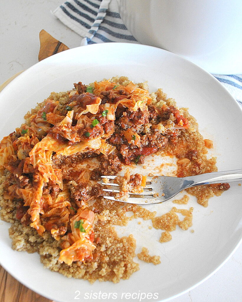 A white plate with cooked quinoa served with cabbage and ground beef on top.