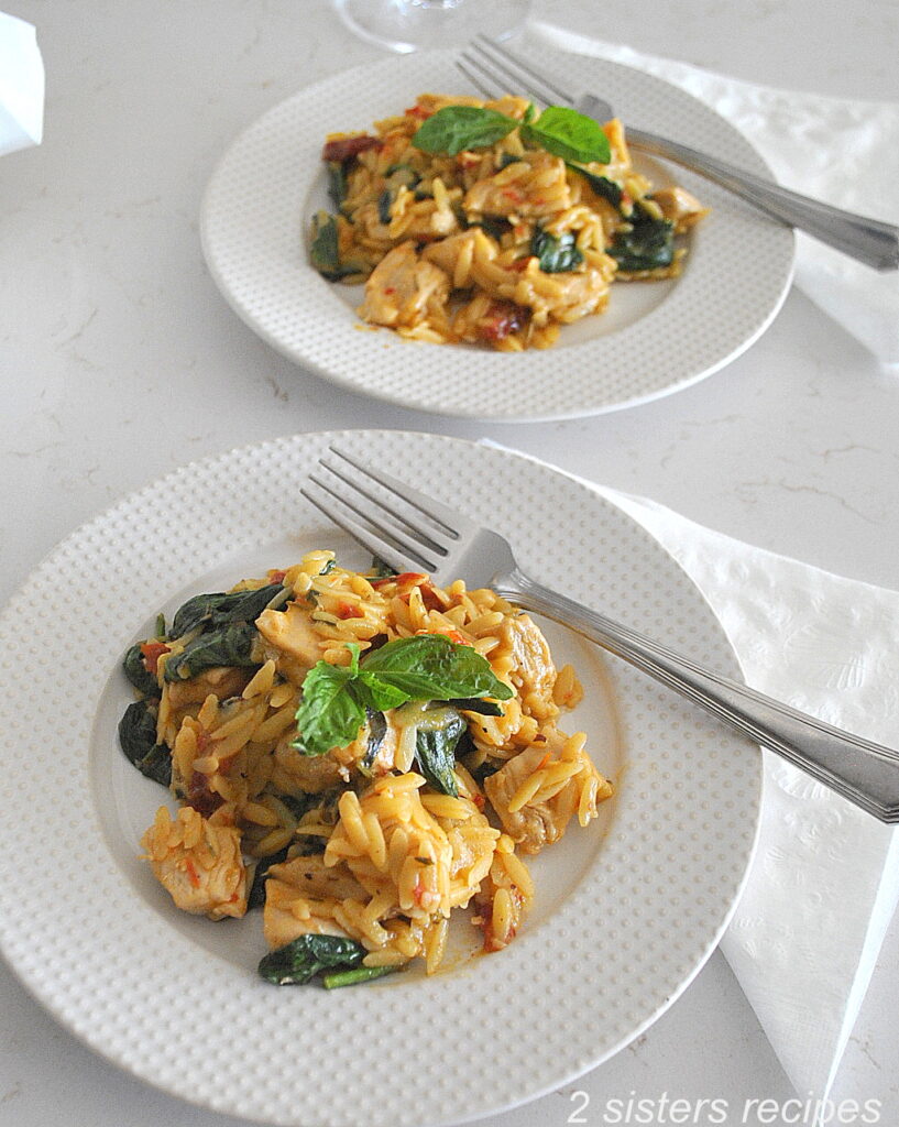 Two white dinner plates with a fork, served with a mixture of orzo, chicken , spinach and cheese.