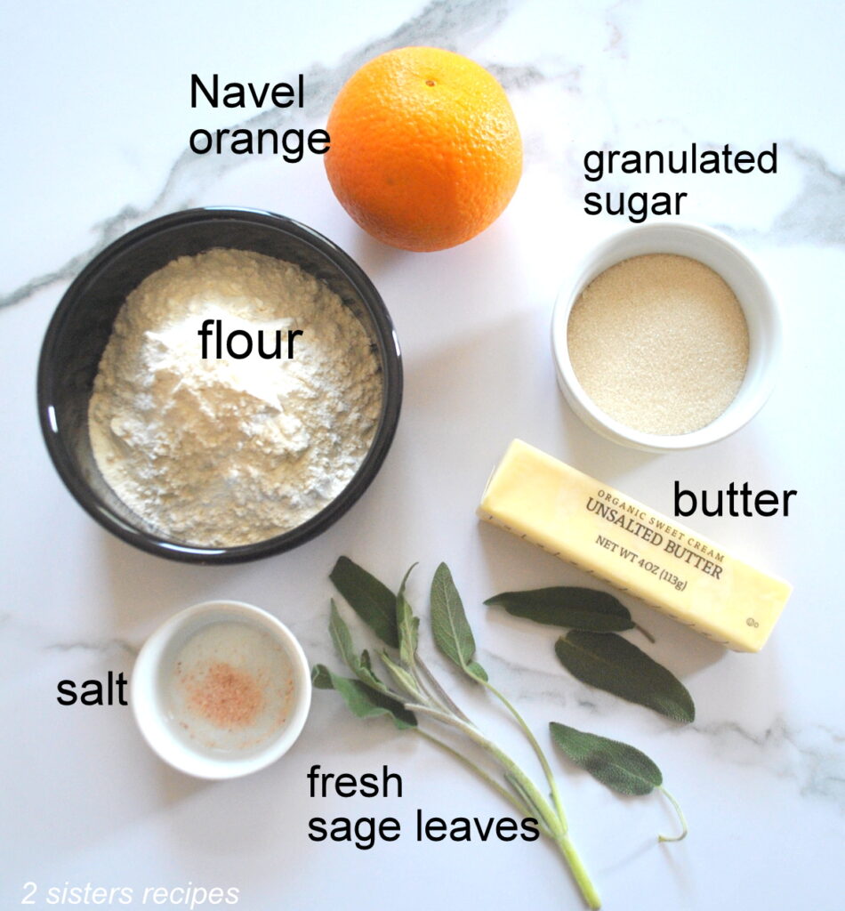 All the ingredients are laid on the counter for these cookies, navel orange, sage leaves, flour, sugar, salt and butter.