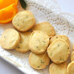 A white platter filled with baked shortbread cookies and 2 orange slices on the side.