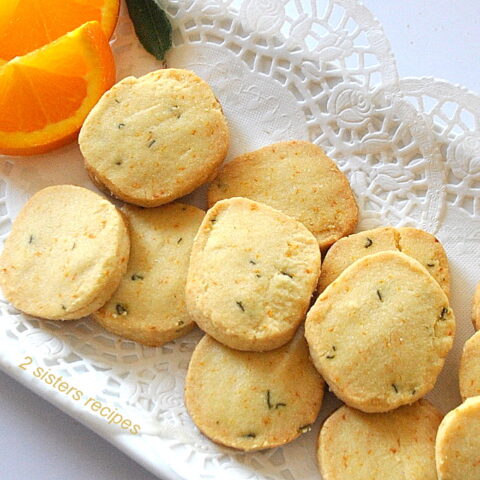 A white platter filled with baked shortbread cookies and 2 orange slices on the side.