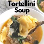 A white bowl and a spoonful of tortellini , spinach and sausage soup.