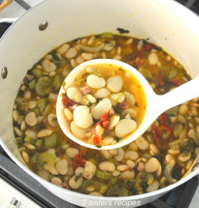 A ladle over a Dutch oven pot filled with a butter beans soup.