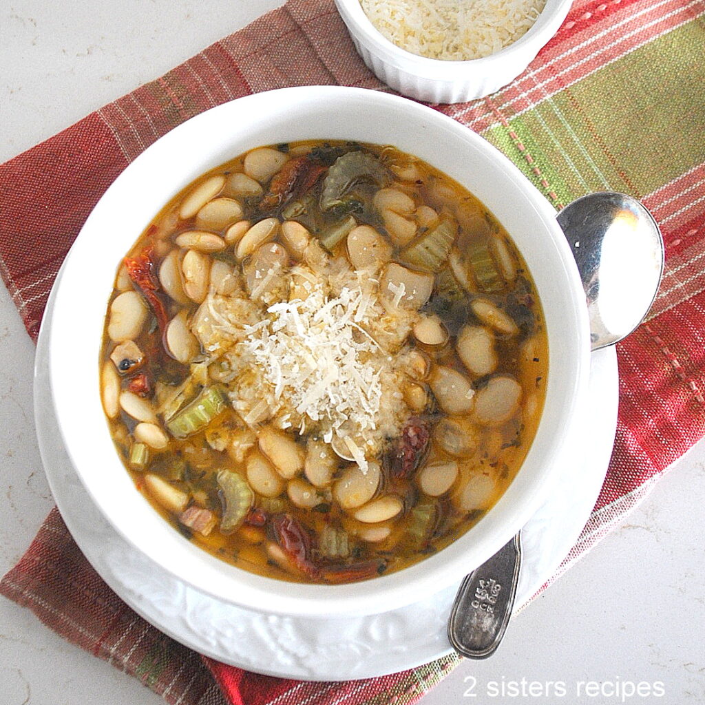 A white bowl filled with a butter beans and veggies soup, topped with grated Parmesan cheese.