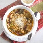 A white bowl filled with a butter beans and veggies soup, topped with grated Parmesan cheese.