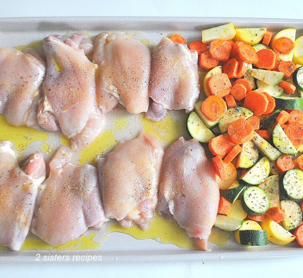 A large sheet pan filled with raw chicken tighs, and chopped veggies, seasoned and with olive oil.