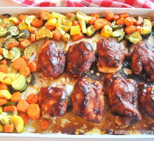 A large sheet pan filled with baked barbecue chicken thighs and mixture of veggies.