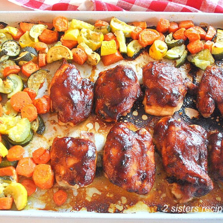 A large sheet pan filled with baked barbecue chicken thighs and mixture of veggies.