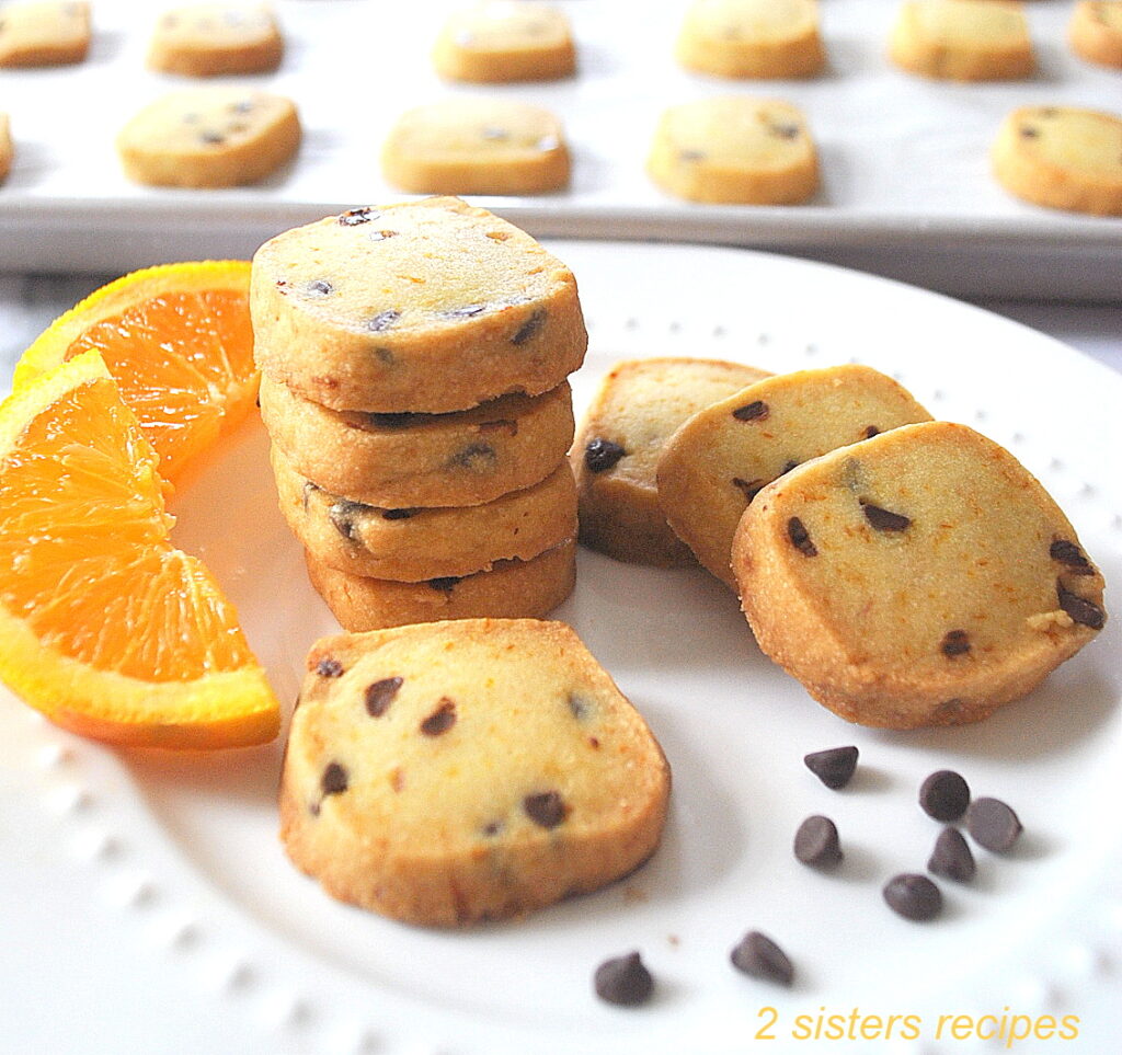 White plate with a pile of small square cookies filled with mini chips inside and scattered on the plate.