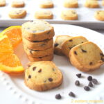 White plate with a pile of small square cookies filled with mini chips inside and scattered on the plate.