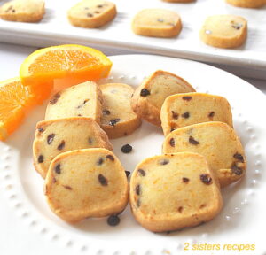 A white plate with small square orange chocolate chip shortbread cookies with slices of orange on the side..