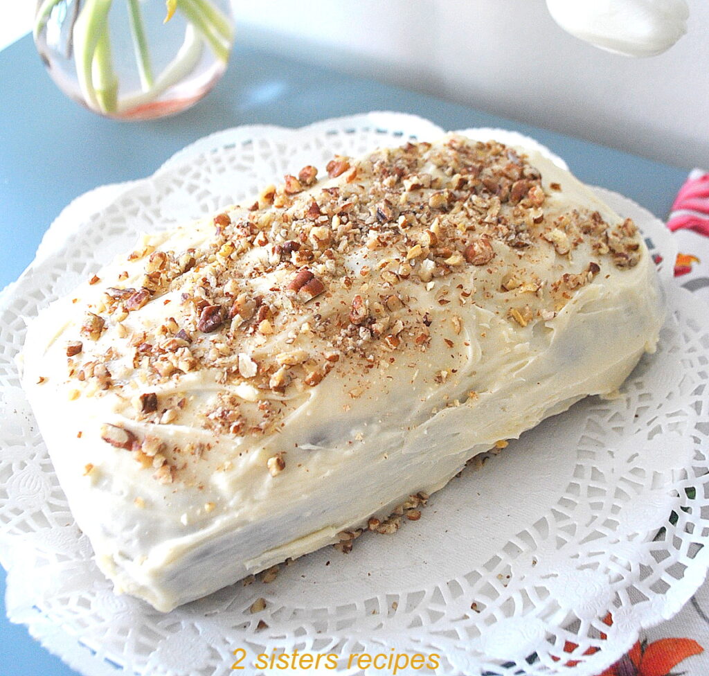 A quick bread topped with a white frosting and crushed pecans served on a white doily.
