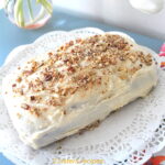 A quick bread topped with a white frosting and crushed pecans served on a white doily.
