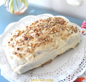 A quick bread topped with a white frosting and crushed pecans served on a white doily.
