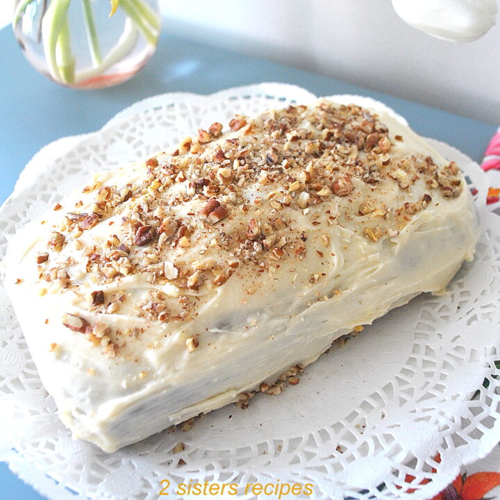 A quick bread topped with a white frosting and crushed pecans served on a white doily.
