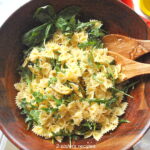 A wooden salad bowl filled with farfalle pasta, and arugula.