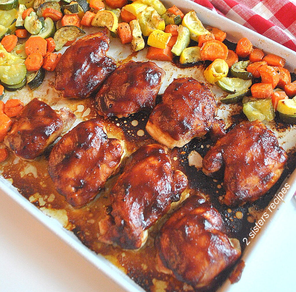 A large sheet pan with baked barbecue chicken thighs, and mixture of vegetables.