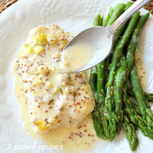 A baked cod fish served with a lemon sauce and asparagus on a white plate.