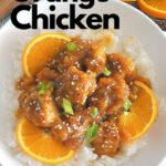 A white bowl filled witth Orange chicken over a bed of white rice. with sliced oranges as garnish.