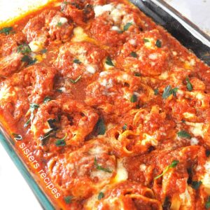 A casserole dish filled with curly pasta smothered with tomato sauce and baked.