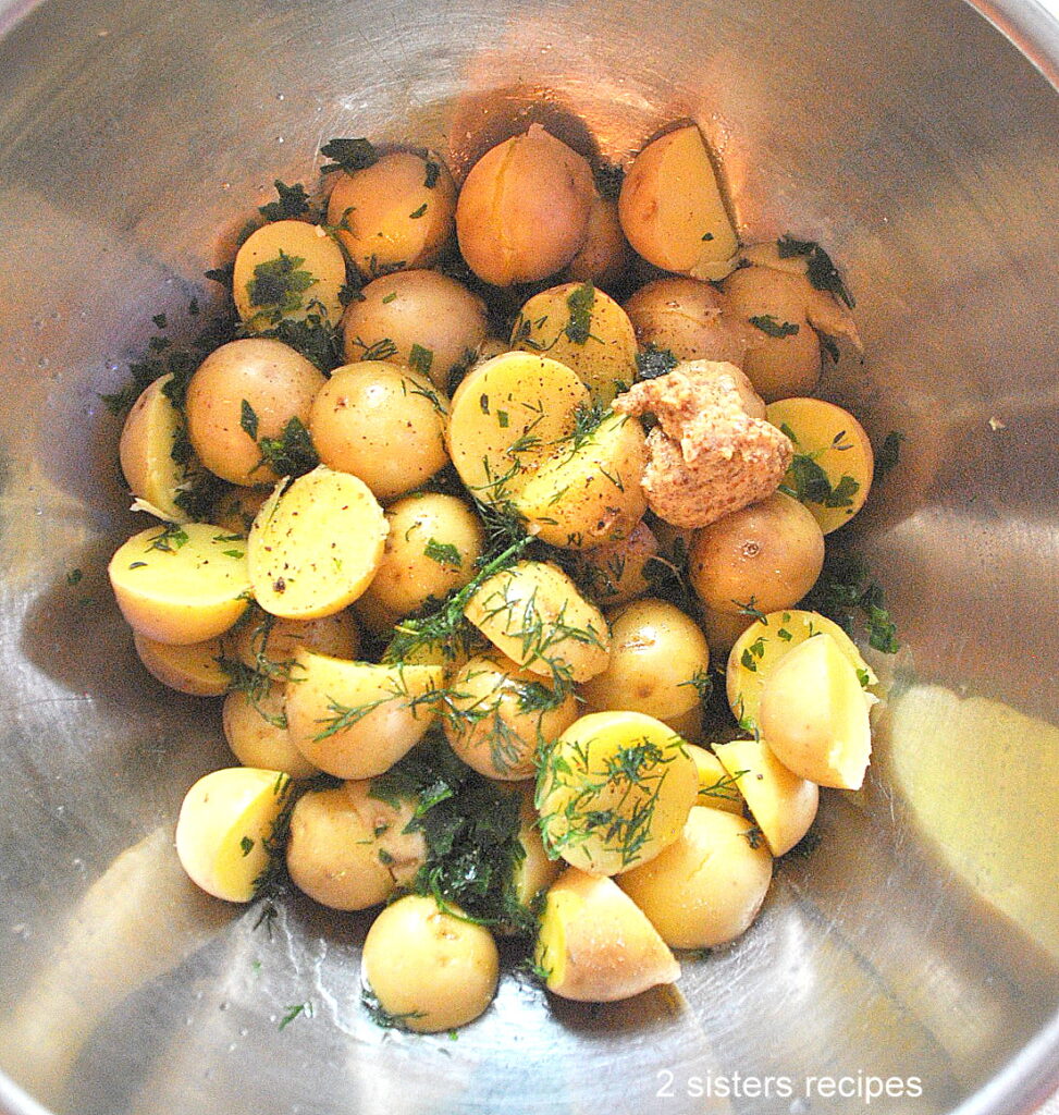 A silver mixing bowl with small potatoes, fresh herbs and Dijon mustard.