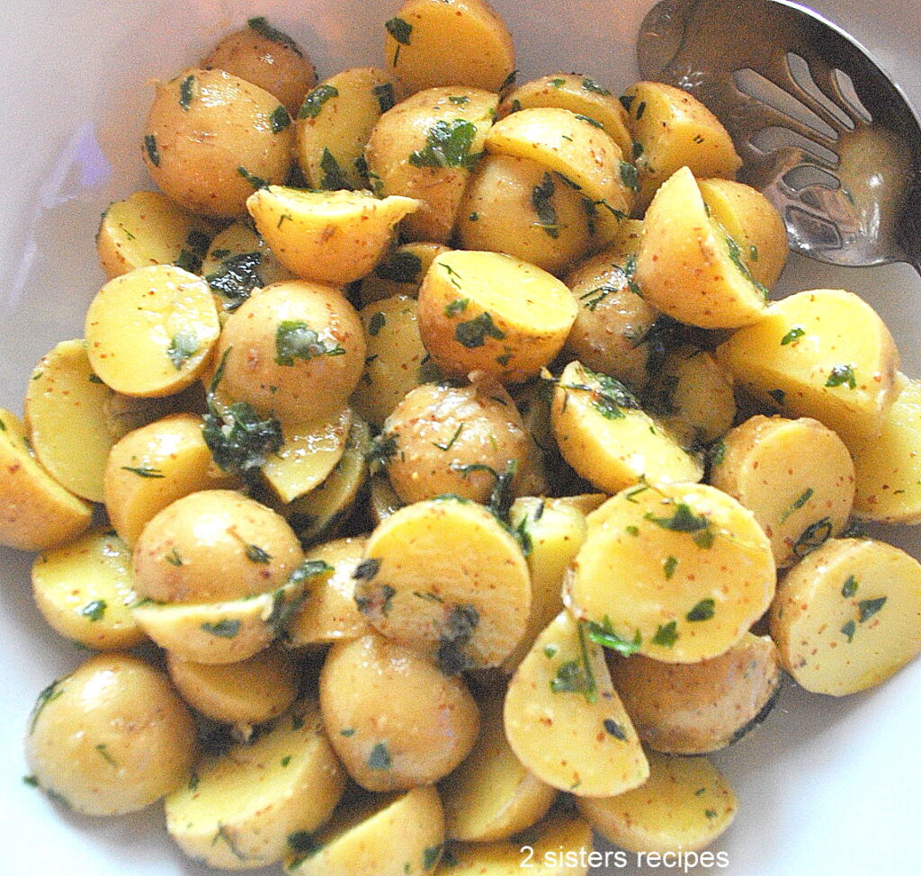 A white salad bowl filled with cut potato salad with fresh herbs.