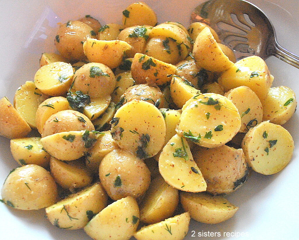 A white salad bowl filled with small potato salad with fresh herbs.