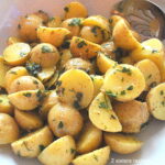 A white salad bowl filled with small potato salad with fresh herbs.