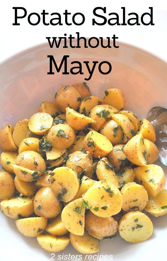 A white salad bowl filled with small cut potatoes salad without mayo.