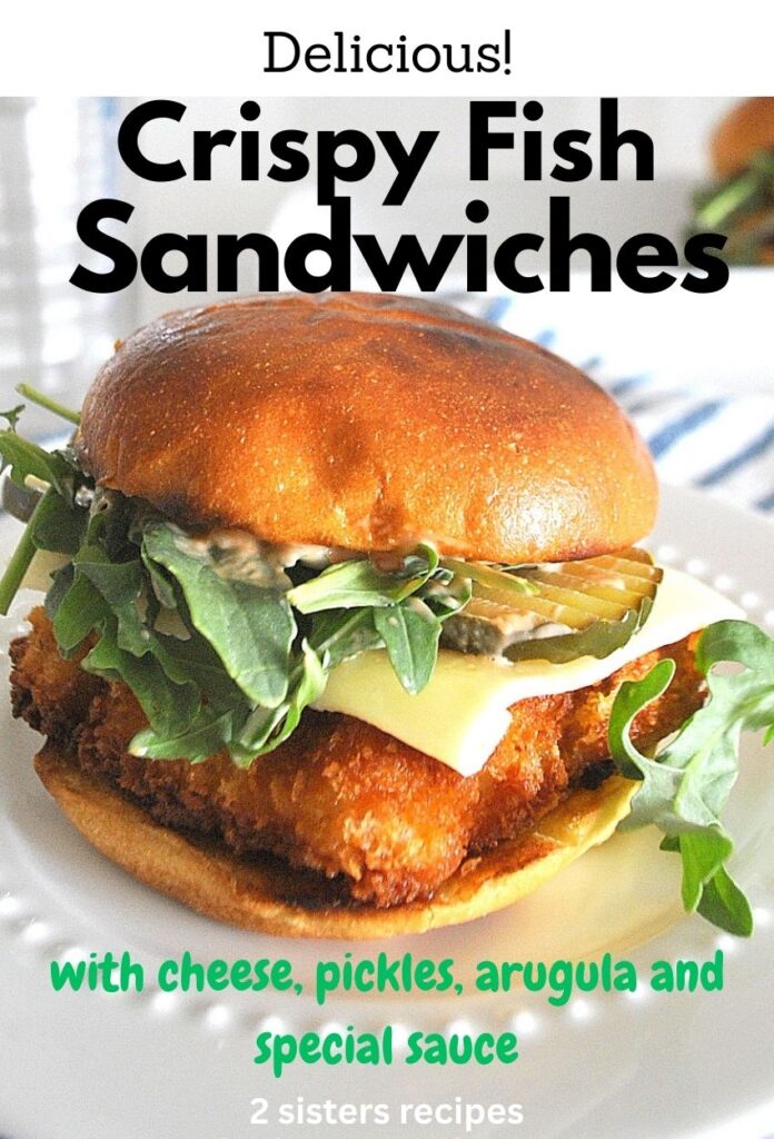 A fish sandwich topped with pickle, arugula, and cheese served on a white plate.