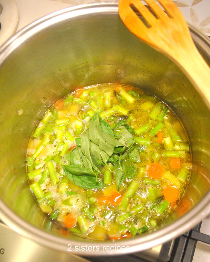 A soup pot filled with freshly chopped veggies, asparagus and fresh basil, simmering on stove top.