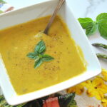 A square bowl filled with asparagus and basil pureed soup.