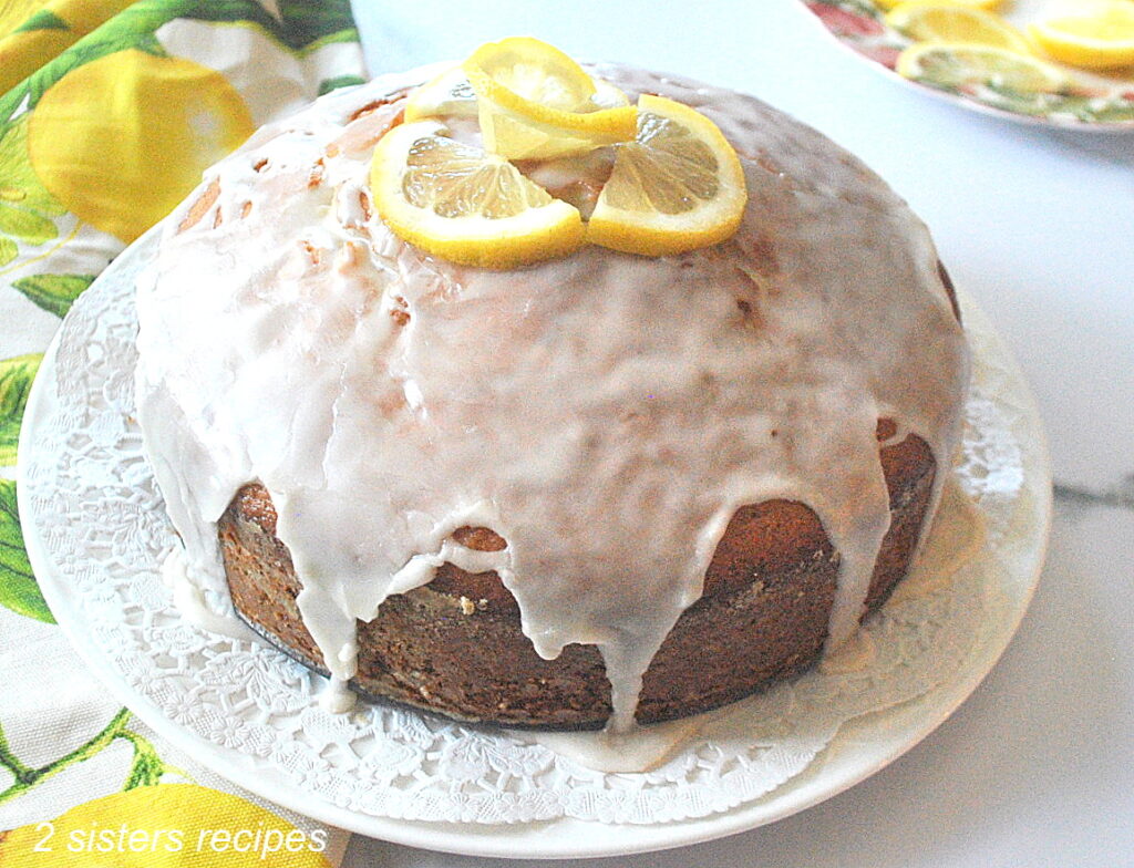 A fully baked cake displayed on a white plate with icing on top and lemon slices.