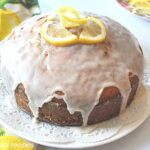 A fully baked cake displayed on a white plate with icing on top and lemon slices.