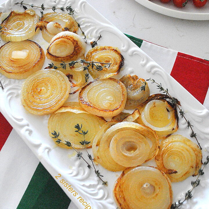 A rectangular white platter filled with caramelized onion rings with sprigs of thyme on the sides.