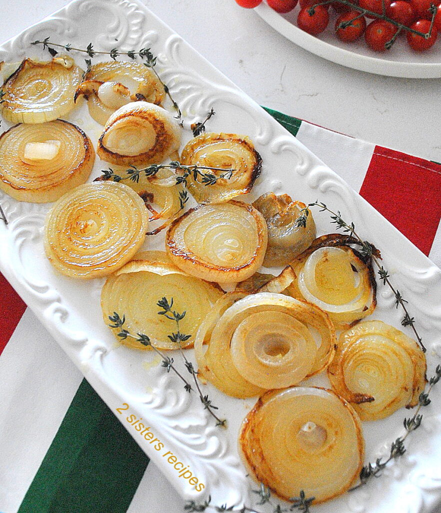 A rectangular white platter filled with caramelized onion rings with sprigs of thyme on the sides.